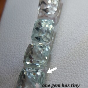 May include: Four light blue aquamarine gemstones, one with a tiny yellow dot, arranged vertically on a white surface.