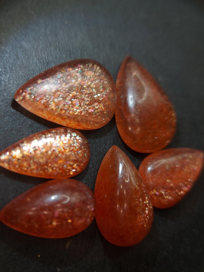 May include: Six teardrop-shaped sunstone cabochons in shades of orange and red with a glittery, iridescent finish.