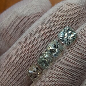 May include: Four faceted, clear, light green gemstones with a square shape. The gemstones are arranged in a row, with the largest gemstone at the top and the smallest gemstone at the bottom.