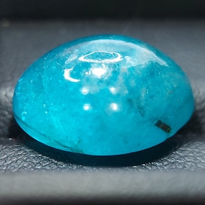 May include: A bright blue, round, cabochon gemstone with a smooth, polished surface. The stone has a slightly cloudy appearance with some inclusions visible.