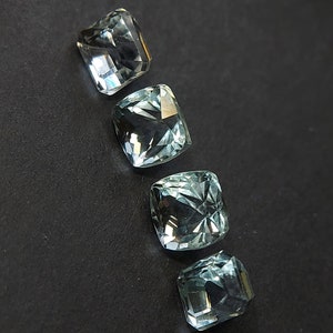May include: Four light blue cushion-cut gemstones on a black background.