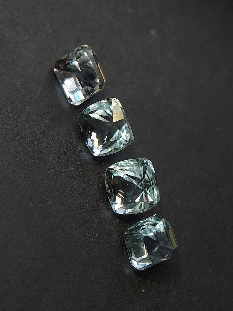 May include: Four light blue cushion-cut gemstones on a black background.