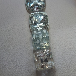 May include: Four clear, faceted, cushion-cut gemstones in various shades of blue and white. The gemstones are arranged vertically, with the largest at the top and the smallest at the bottom.
