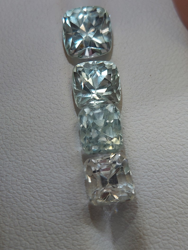 May include: Four clear, faceted, cushion-cut gemstones in various shades of blue and white. The gemstones are arranged vertically, with the largest at the top and the smallest at the bottom.