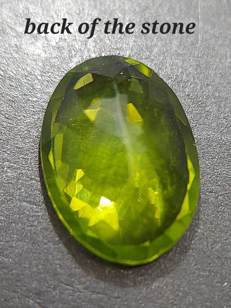 Peut inclure: Gros plan sur le dos d'une pierre pr&eacute;cieuse verte. La pierre est de forme ovale et a une taille facet&eacute;e. La pierre r&eacute;fl&eacute;chit la lumi&egrave;re, cr&eacute;ant un effet brillant et lumineux.
