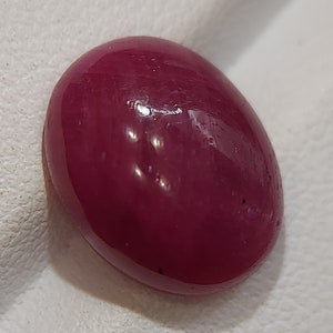 May include: A deep red oval-shaped gemstone with a smooth, polished surface.