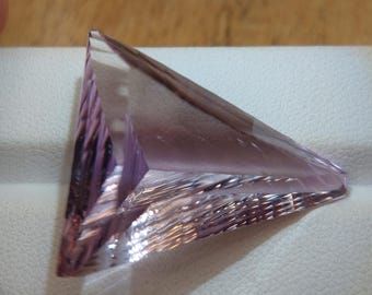 May include: A triangular, faceted, clear crystal with a light purple hue. The crystal is cut with many facets and has a smooth, polished surface.