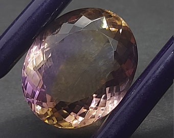 May include: A faceted oval-shaped gemstone with a purple and brown color gradient. The gemstone is held by a pair of tweezers.