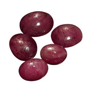 May include: Five oval-shaped, red star ruby gemstones. The stones have a deep red colour and a star-like pattern.