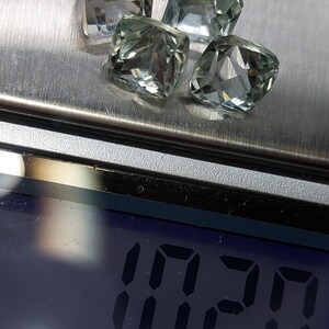 May include: Four clear green gemstones, likely amethysts, are arranged on a silver surface. A digital scale displays "1.20 ct" indicating the total weight of the gemstones.