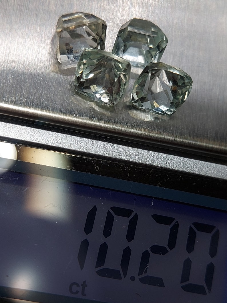 May include: Four clear green gemstones, likely amethysts, are arranged on a silver surface. A digital scale displays "1.20 ct" indicating the total weight of the gemstones.