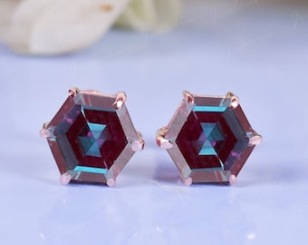 May include: A pair of hexagonal shaped earrings with a dark purple and blue gemstone set in a rose gold setting.