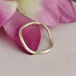 Könnte beinhalten: Ein einfacher Silberring mit abgerundeter, leicht quadratischer Form. Der Ring wird auf einem rosa Hintergrund gezeigt.