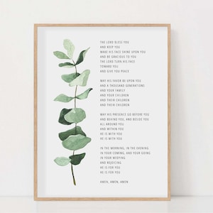 Op de afbeelding: Een ingelijst print met een aquarel-illustratie van een eucalyptus tak. De print bevat een religieuze tekst over zegeningen en vrede. De tekst luidt: "De Heer zegene u en bewaar u. Hij laat zijn aangezicht over u schijnen en is u genadig. De Heer wende zijn aangezicht naar u en schenke u vrede. Zijn gunst zij over u en over duizend geslachten, over uw gezin, over uw kinderen, over hun kinderen en over hun kinderen. Zijn tegenwoordigheid ga voor u uit en volg u na, zij zij aan uw rechterhand en aan uw linkerhand, zij omhulle u en zij in u. Hij is met u. Hij is met u. In de morgen, in de avond, bij uw komen en bij uw gaan, in uw tranen en in uw vreugde. Hij is voor u. Hij is voor u. Amen, Amen, Amen."