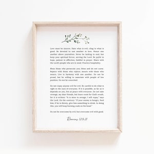 May include: A white framed print with a green watercolour floral design in the top left corner. The print features a quote from Romans 12:9-21 about love, hate, and overcoming evil with good.