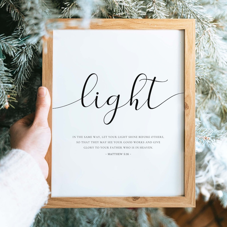 Może przedstawiać: Biały wydruk w ramie z napisem "light" w ozdobnym, pochylonym piśmie. Wydruk zawiera werset biblijny z Ewangelii Mateusza 5:16: "Tak niech świeci wasze światło przed ludźmi, aby widzieli wasze dobre uczynki i chwalili Ojca waszego, kt&oacute;ry jest w niebie."