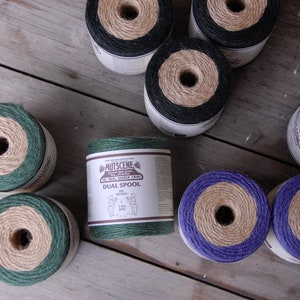Könnte beinhalten: Sortiment von Garnrollen in Grün, Schwarz und Lila mit Naturgarn. Die Rollen sind mit "Nutscene" und "Dual Spool" beschriftet.