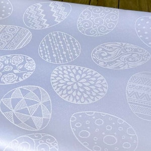 May include: A light blue tablecloth with a white pattern of various Easter eggs. The eggs have different designs, including floral, geometric, and abstract patterns.