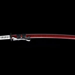 Pode incluir: Uma katana, espada japonesa tradicional, com uma lâmina branca e preta e uma bainha laqueada de vermelho.