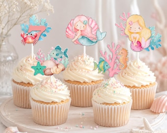 May include: A set of five cupcakes topped with paper decorations featuring watercolor illustrations of mermaids, a crab, a seahorse, fish, coral, and a large number seven. Each topper is attached to a white stick inserted into the frosting.