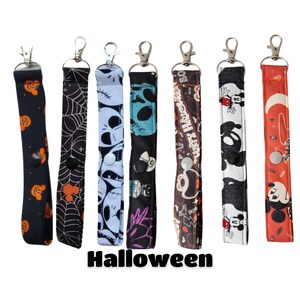 May include: Set of eight Halloween-themed lanyard keychains. The lanyards feature various designs including Mickey Mouse, a spiderweb, a skull, a ghost, and a spooky Halloween message. Each lanyard has a black button and a silver clip.