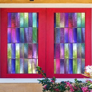 May include: A red window frame with two panes of stained glass. The glass is made up of small, rectangular pieces in shades of purple, blue, green, and yellow.