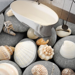 以下が含まれることがあります： 白いバスタブが、グレーの石と白い貝殻で覆われた床の上に置かれています。バスタブはグレーのタオルで部分的に覆われています。