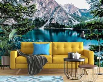 May include: A yellow sofa with a grey throw blanket and a blue cushion sits in front of a wall mural depicting a mountain lake scene. The lake is surrounded by snow-capped mountains and lush green trees.