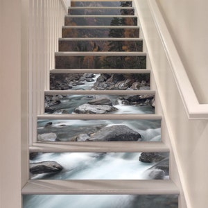 Puede incluir: Un conjunto de 7 peldaños de escalera con un diseño de río y rocas escénico. Los peldaños son blancos y el diseño está impreso en la superficie. El diseño presenta un río que fluye con rocas y un bosque en el fondo.