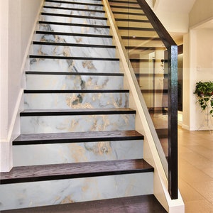 May include: A set of white marble stair treads with gold veining. The treads are installed on a set of wooden stairs with a black handrail.