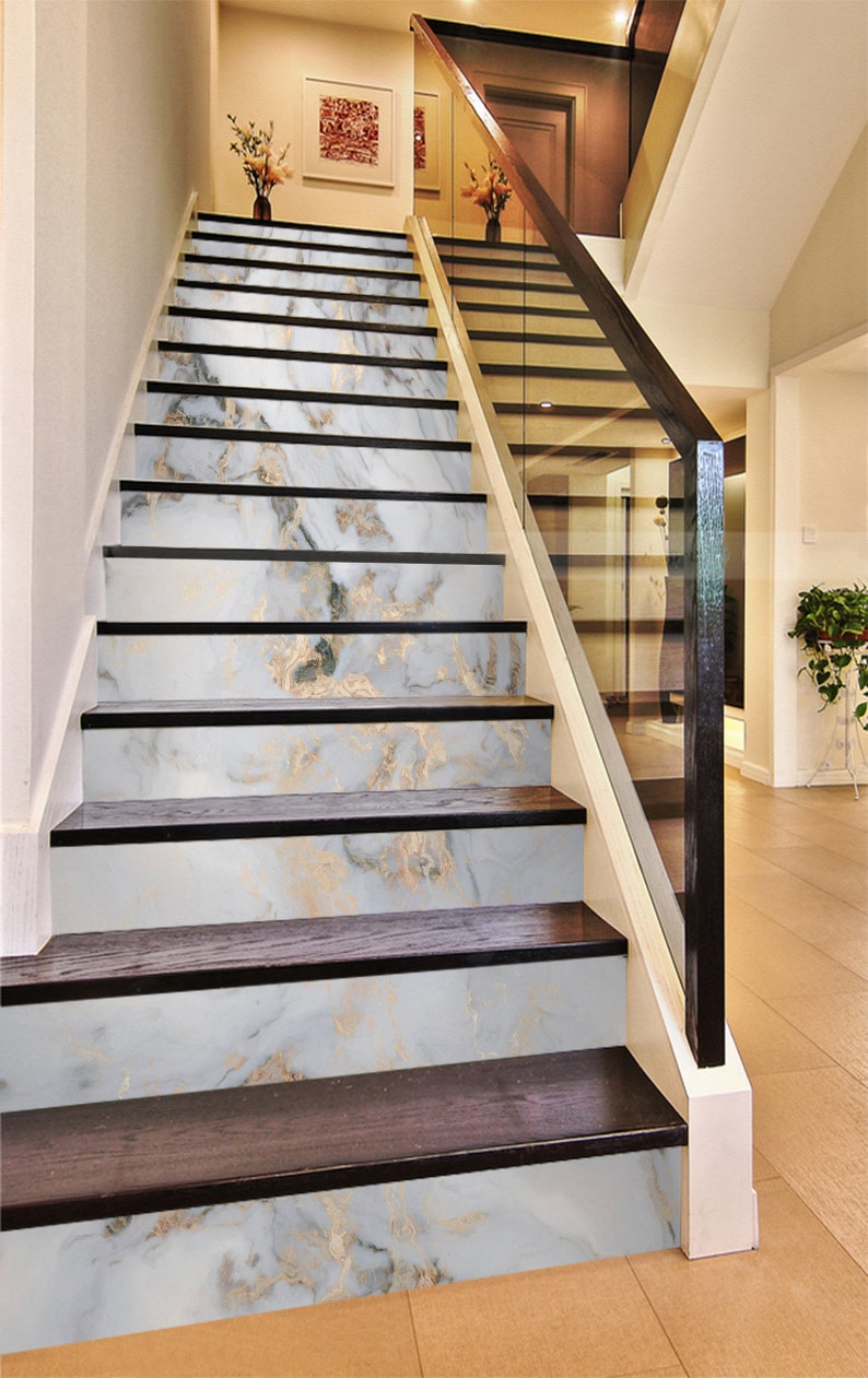 May include: A set of white marble stair treads with gold veining. The treads are installed on a set of wooden stairs with a black handrail.