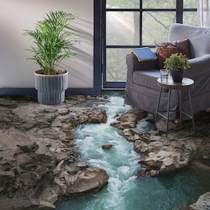 Puede incluir: Una sala de estar con un sillón gris, una mesa auxiliar y una planta en maceta. El suelo está cubierto con una alfombra impresa en 3D que parece un río embravecido con rocas.