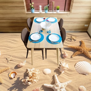 Könnte beinhalten: Ein Esstisch mit vier Stühlen auf einem Strand-Boden. Der Boden ist mit Sand bedeckt, auf dem sich Seesterne, Muscheln und Korallen befinden. Der Tisch ist aus Holz und hat eine hellbraune Oberfläche. Auf dem Tisch befinden sich vier Gedecke, jedes mit einem weißen Teller, einem blauen Platzdeckchen und einer silbernen Gabel und einem Messer.