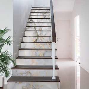 May include: White and gold marble-patterned stair treads with dark brown wood risers. The stairs are in a modern home with white walls and a white railing.