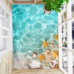 Può includere: Un rivestimento per pavimenti blu e bianco con una scena di spiaggia. Il rivestimento per pavimenti presenta un oceano blu con onde bianche, conchiglie e stelle marine.