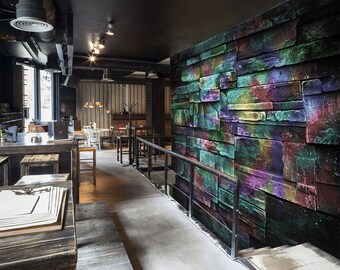 May include: A modern restaurant interior with a black ceiling and exposed ductwork. A long wooden bar with stools is in the foreground. The wall behind the bar is covered in a colourful, abstract mural of stacked stone blocks.