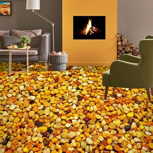 May include: A close-up of a patterned floor covering that looks like a pile of small, yellow, orange, and brown pebbles. The floor is in a living room with a couch, a lamp, and a fireplace.