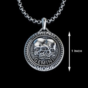 May include: Silver pendant necklace featuring a skull with two faces, the text "Memento Mori Gemini" is inscribed around the skull. The pendant is 1 inch in diameter.