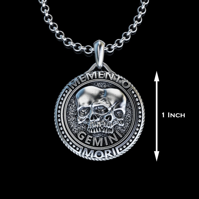 May include: Silver pendant necklace featuring a skull with two faces, the text "Memento Mori Gemini" is inscribed around the skull. The pendant is 1 inch in diameter.