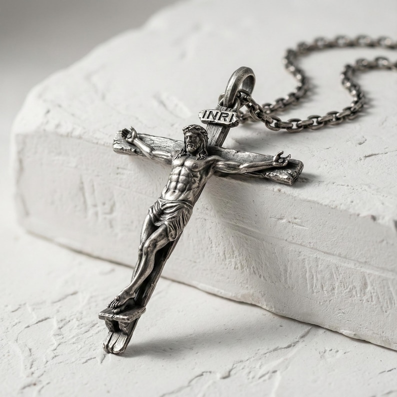 Puede incluir: Colgante de crucifijo plateado con una detallada representaci&oacute;n de Jes&uacute;s en la cruz, colgado de una cadena a juego. La cruz lleva la inscripci&oacute;n "INRI" en la parte superior.
