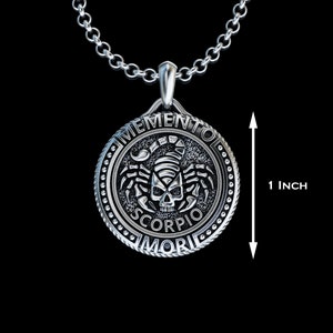 May include: Silver pendant necklace with a round charm featuring a scorpion skull design and the text "Memento Mori Scorpio". The charm is 2.5 cm in diameter.