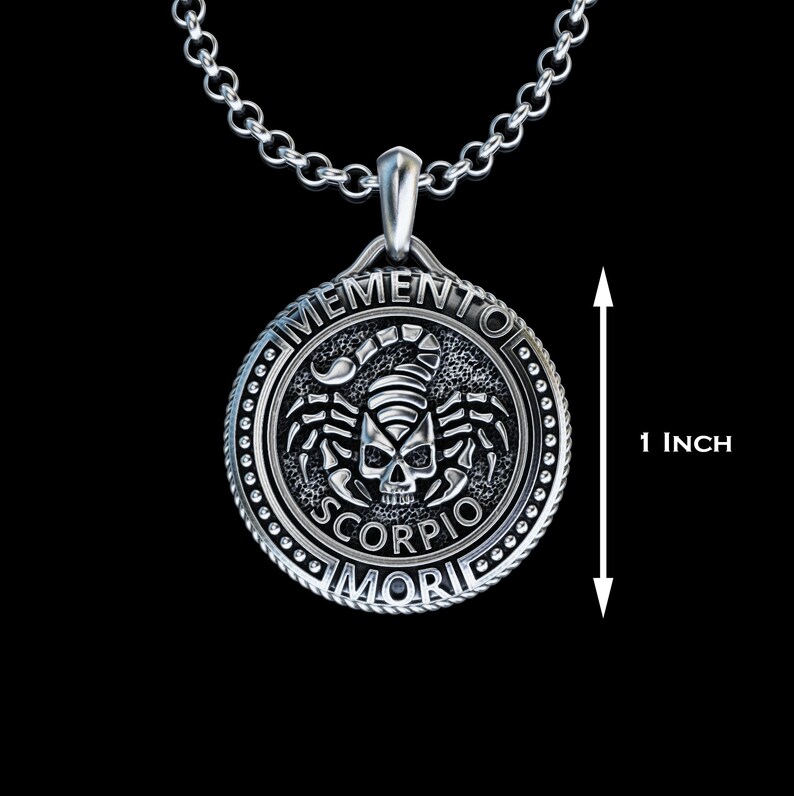 May include: Silver pendant necklace with a round charm featuring a scorpion skull design and the text "Memento Mori Scorpio". The charm is 2.5 cm in diameter.