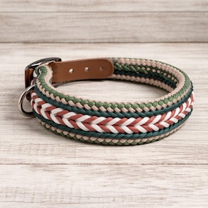 May include: Braided dog collar with a brown leather buckle and a metal D-ring. The collar features a woven design in shades of green, white, and red. The collar is approximately 1 inch wide.