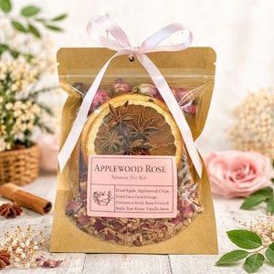 May include: A kraft paper bag containing an "Applewood Rose Simmer Pot Kit" tied with a pink ribbon. The kit includes dried apple, orange slices, star anise, cinnamon sticks, rose petals, and vanilla bean.