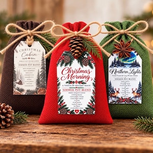 May include: Three textured fabric pouches in brown, red, and green, each tied with twine and a decorative tag. The tags feature labels for Christmas Cabin, Christmas Morning, and Northern Lights simmer pot blends, listing ingredients like dried fruit.