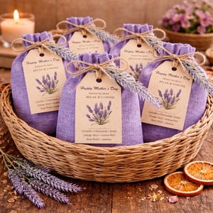 May include: A woven basket holds several small, purple fabric bags tied with twine and tags that read "Happy Mother's Day." Each bag features a lavender sprig and a list of ingredients. Dried orange slices and lavender sprigs are arranged around the basket.