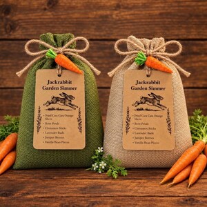 May include: Two burlap drawstring bags, one olive green and one tan, each tied with a small orange carrot. A rectangular kraft paper tag on each bag reads Jackrabbit Garden Simmer and lists ingredients including dried orange slices and rose petals.