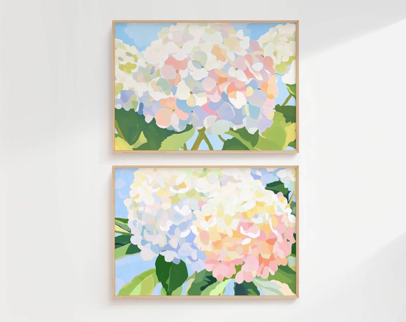 K&ouml;nnte beinhalten: Zwei gerahmte florale Kunstdrucke. Jeder Druck zeigt eine Nahaufnahme einer Hortensienbl&uuml;te in Wei&szlig;-, Rosa- und Blaut&ouml;nen vor einem hellblauen Hintergrund. Das Kunstwerk ist in hellem Holz gerahmt.