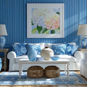 K&ouml;nnte beinhalten: Ein Wohnzimmer mit wei&szlig;em Sofa, blauen Kissen und einem wei&szlig;en Couchtisch. Der Raum hat einen blauen Teppich, blaue Wandpaneele und ein gerahmtes Blumenbild. Zwei geflochtene K&ouml;rbe und Lampen mit blau-wei&szlig;em Muster.