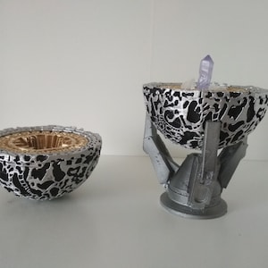 May include: A silver and black sphere with a gold interior, open to reveal a purple crystal. The sphere is on a silver stand with three legs.